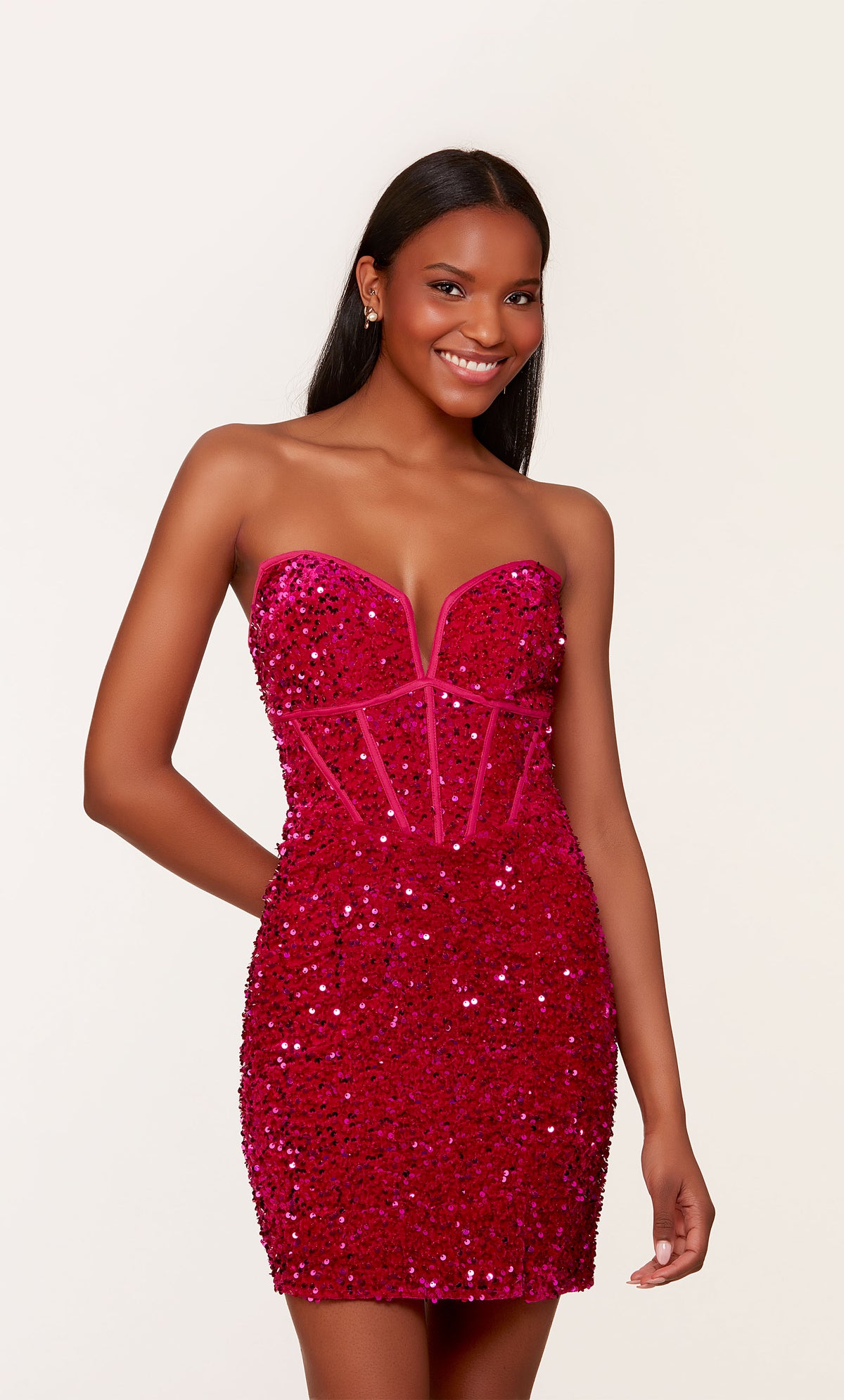 A short corset prom dress in iridescent, raspberry colored sequins. The dress features a strapless neckline, a zipper side slit, and a lace-up back.